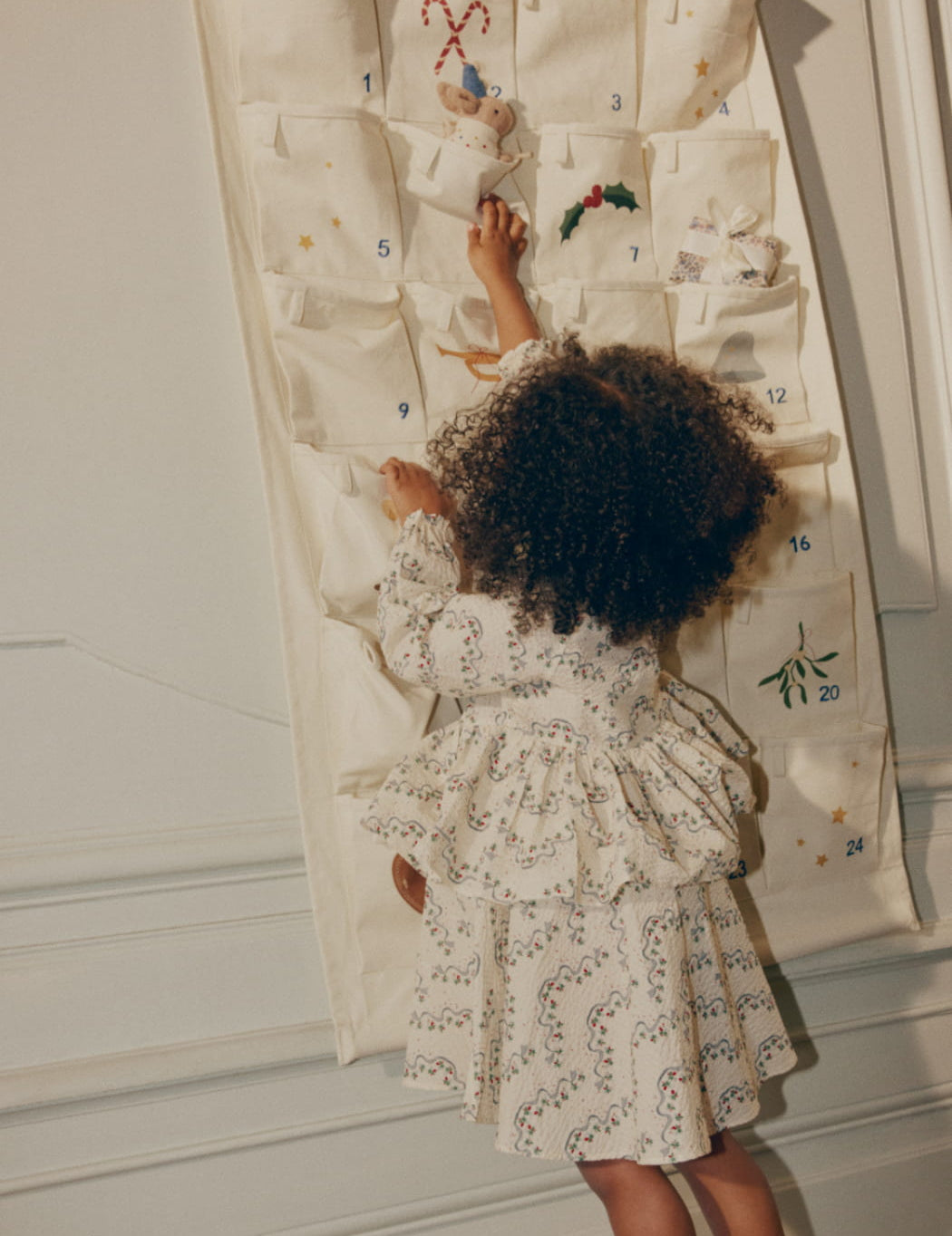 Child in a floral dress interacting with a large Advent calendar.