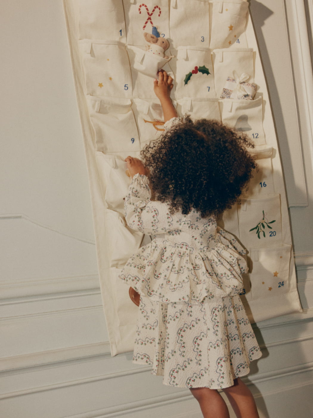Child in a floral dress interacting with a large Advent calendar.
