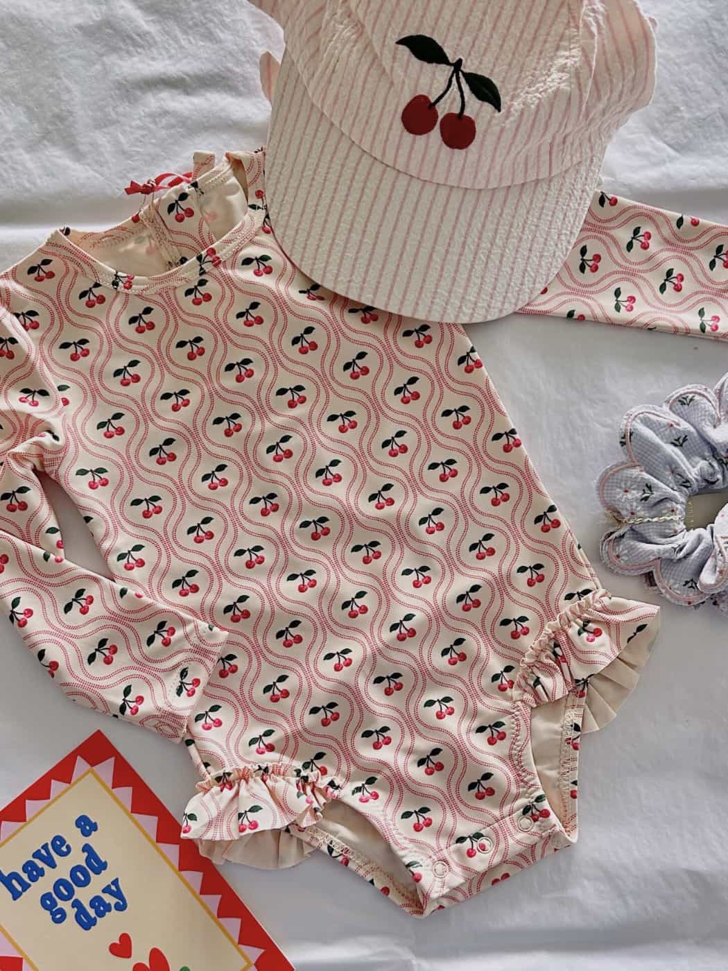 Children's swimsuit with cherry pattern and matching hat on a white background