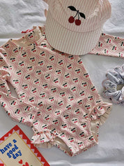 Children's swimsuit with cherry pattern and matching hat on a white background