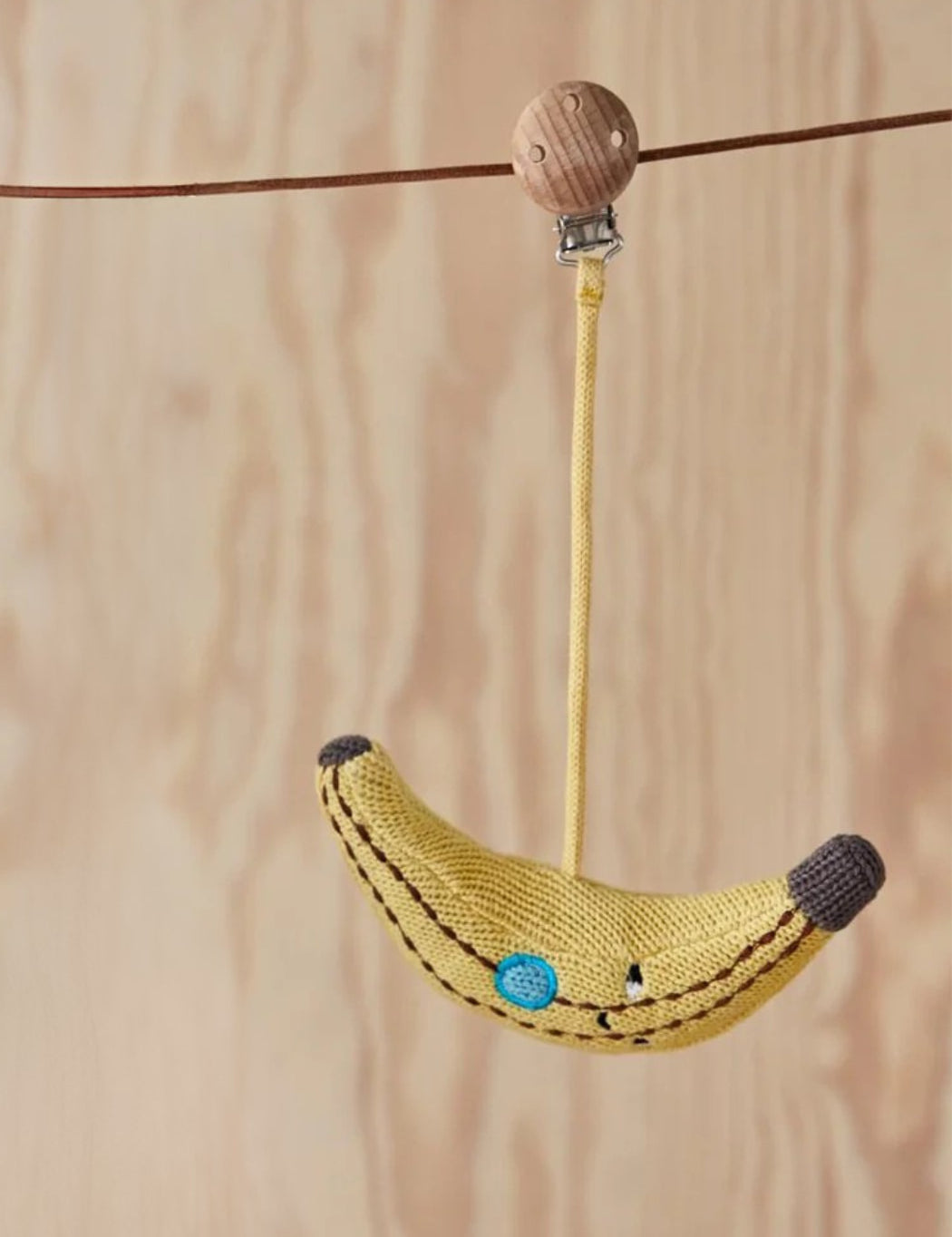 Knitted banana-shaped toy with a wooden bead on a string against a wooden background