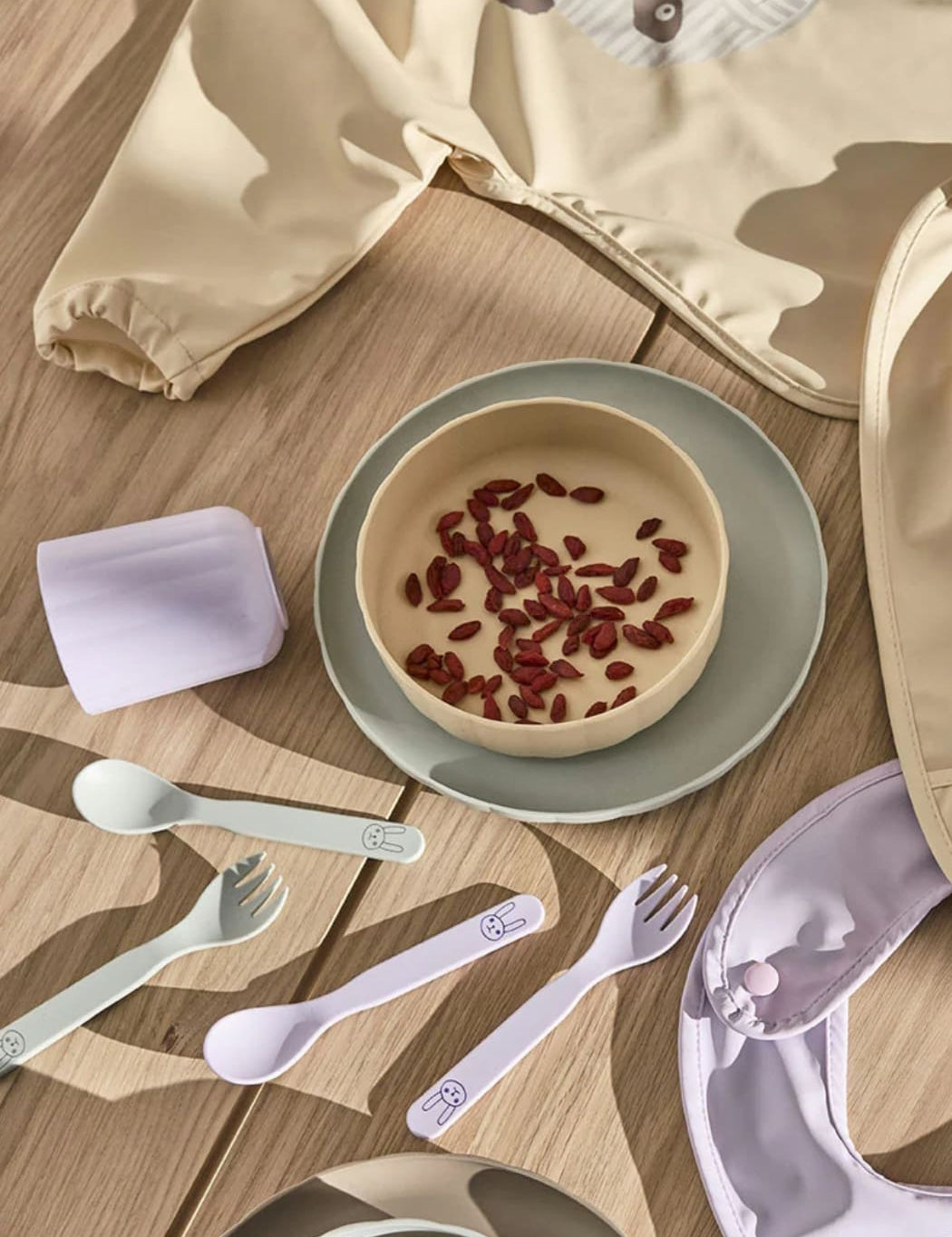 Children's tableware set with bowls, spoons, and forks on a wooden surface.