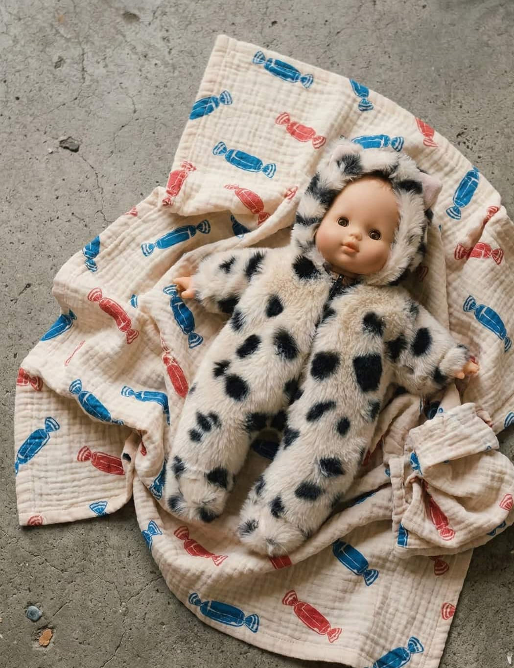 Baby doll in a spotted outfit on a textured blanket with colorful patterns.