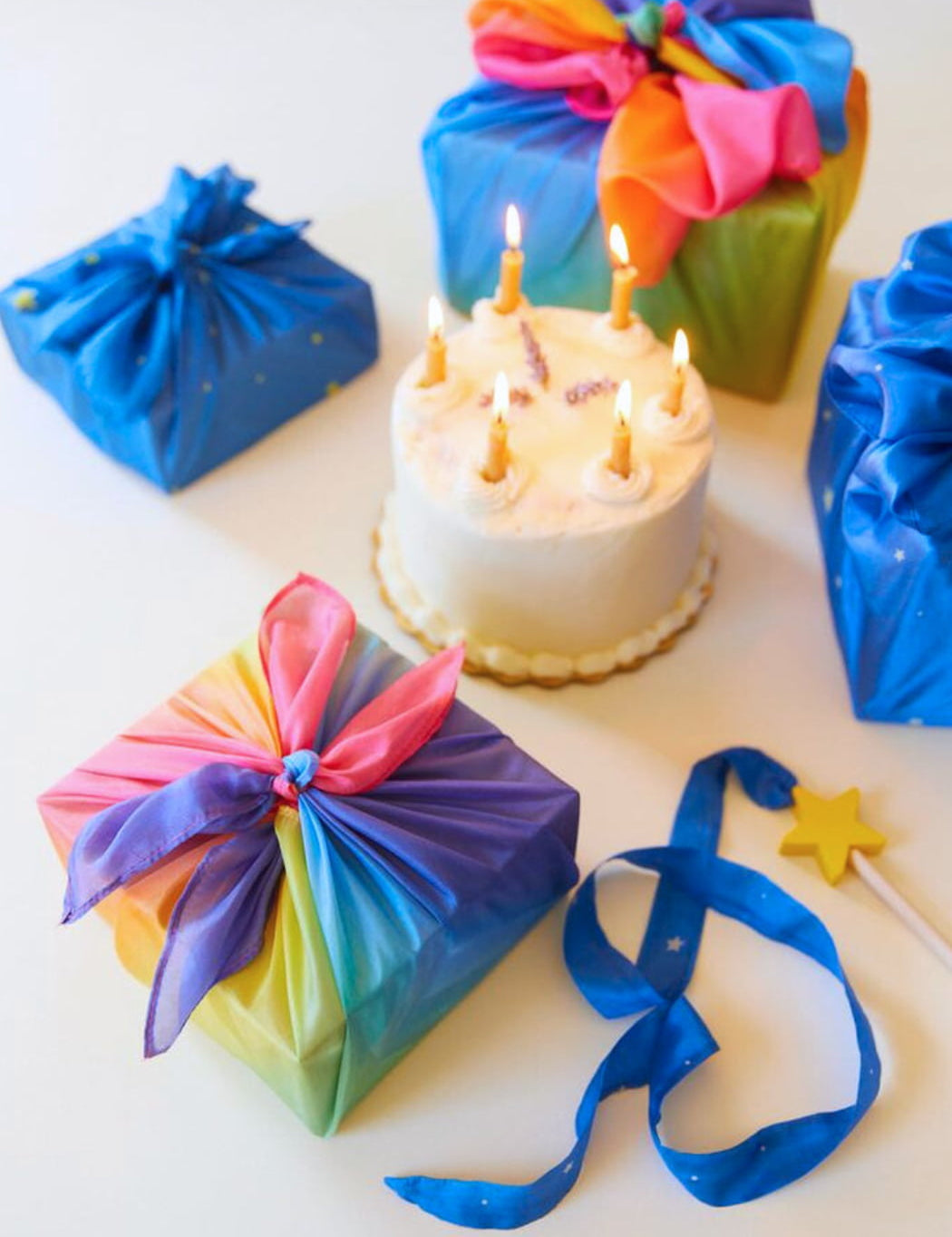 A group of presents wrapped in silk scarves and a birthday cake with candles