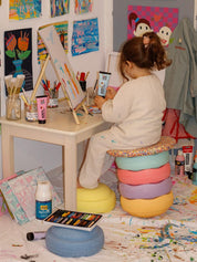 Child sitting at a table with art supplies, surrounded by colorful artwork on the wall.